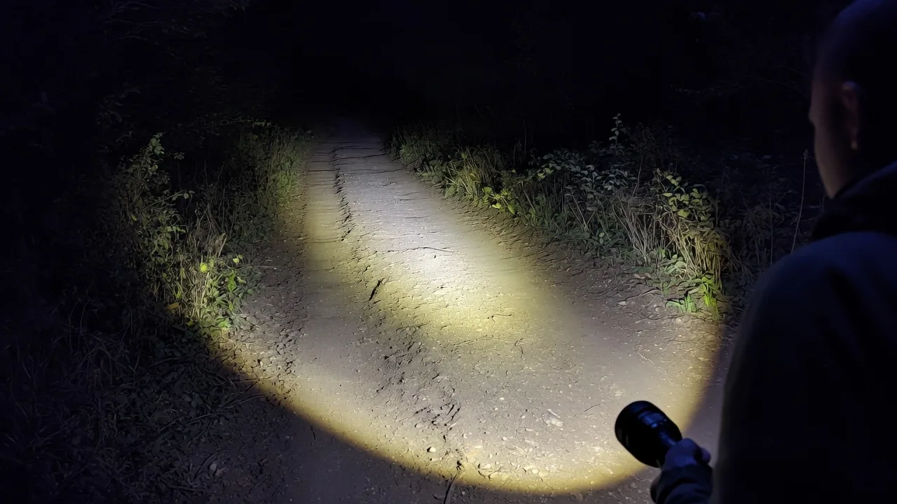 A hiker's flashlight lighting a rutted dirt trail ahead at night, the beam falling off into darkness further along the path.