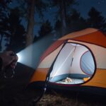 Person using a camping torch to illuminate a tent at night, demonstrating the best camping torches in action